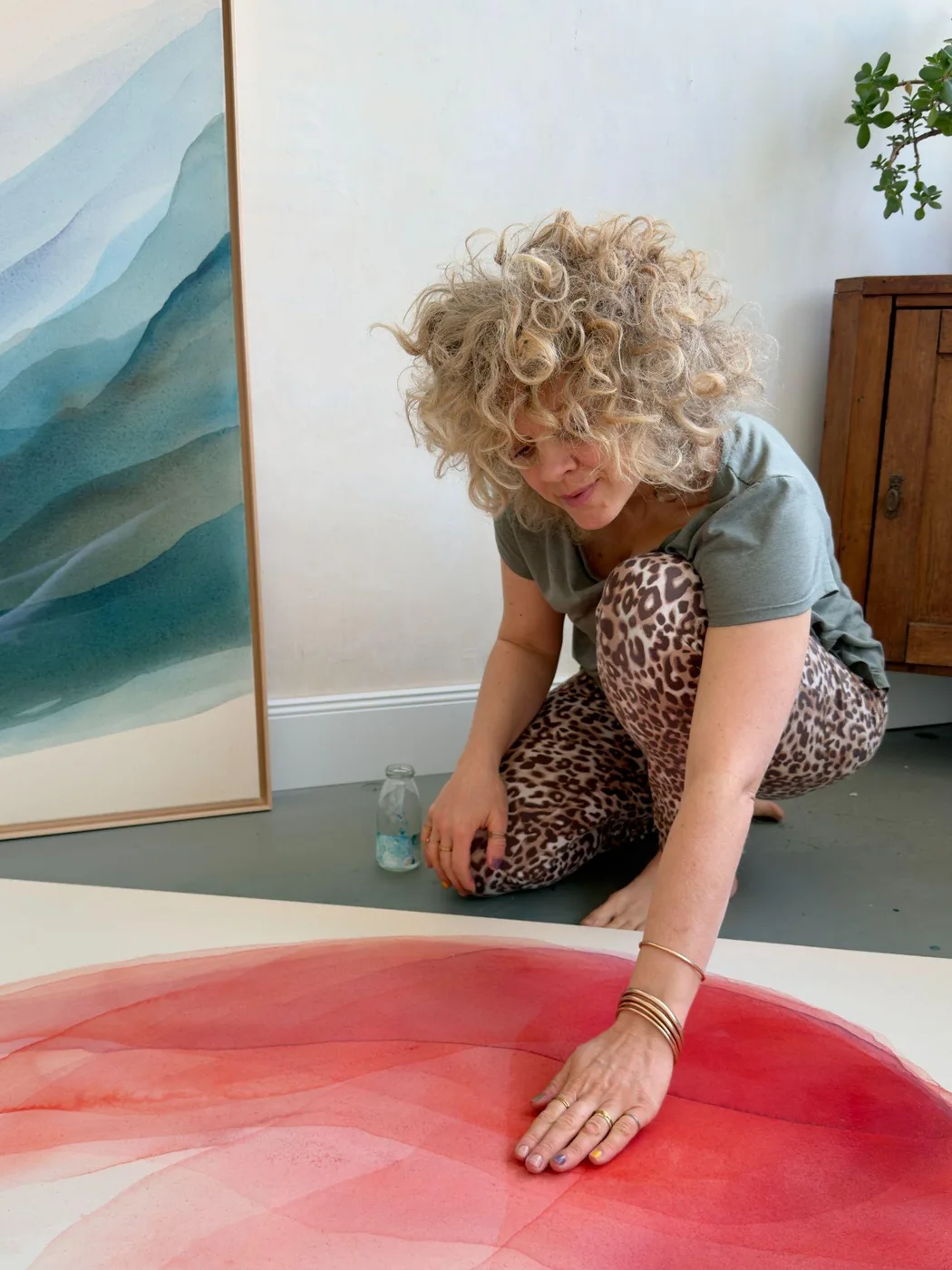 Johanne Bossmann schildert met de hand op een doek in roodtinten, naast een ingelijst werk in blauw