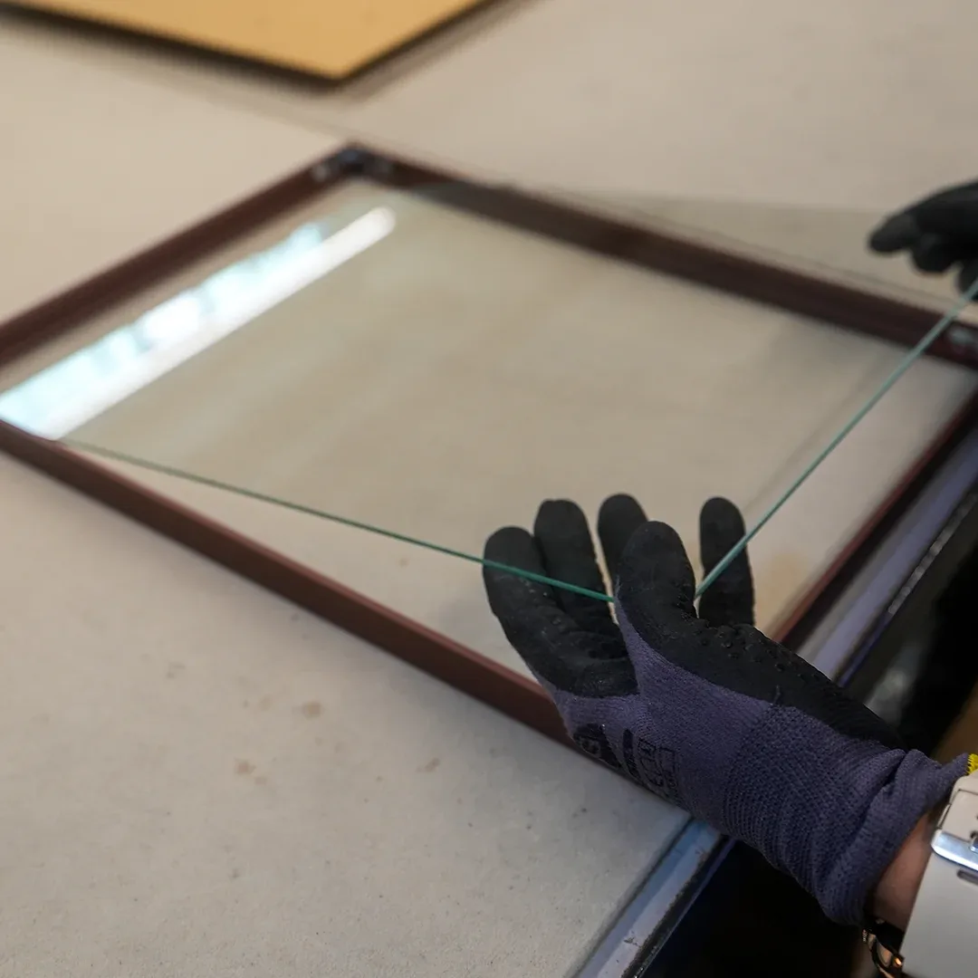 Met veiligheidshandschoenen wordt een glasplaat in een donkere houten lijst gelegd